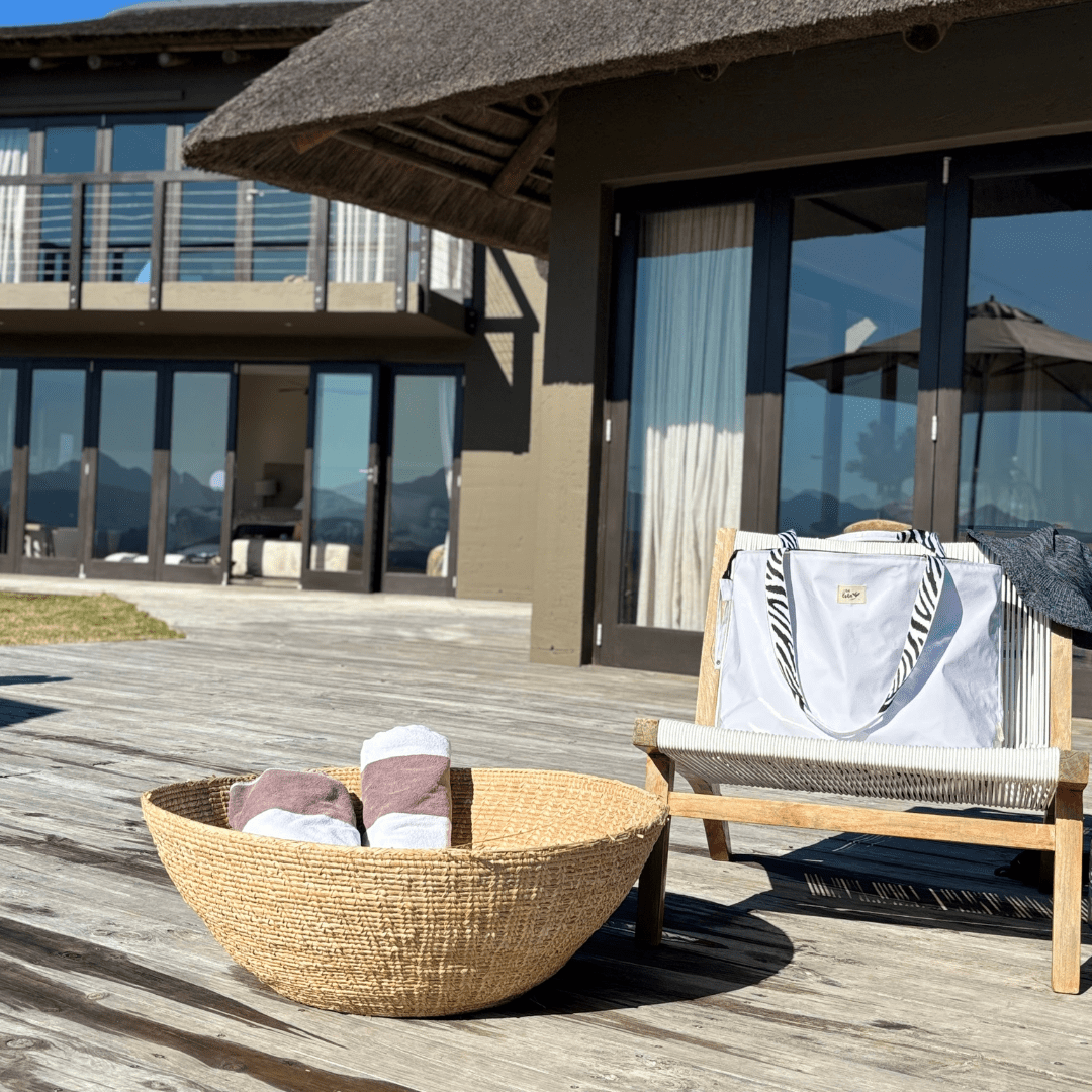 Outdoor wooden deck with woven basket holding towels and white tote bag on chair near modern house
