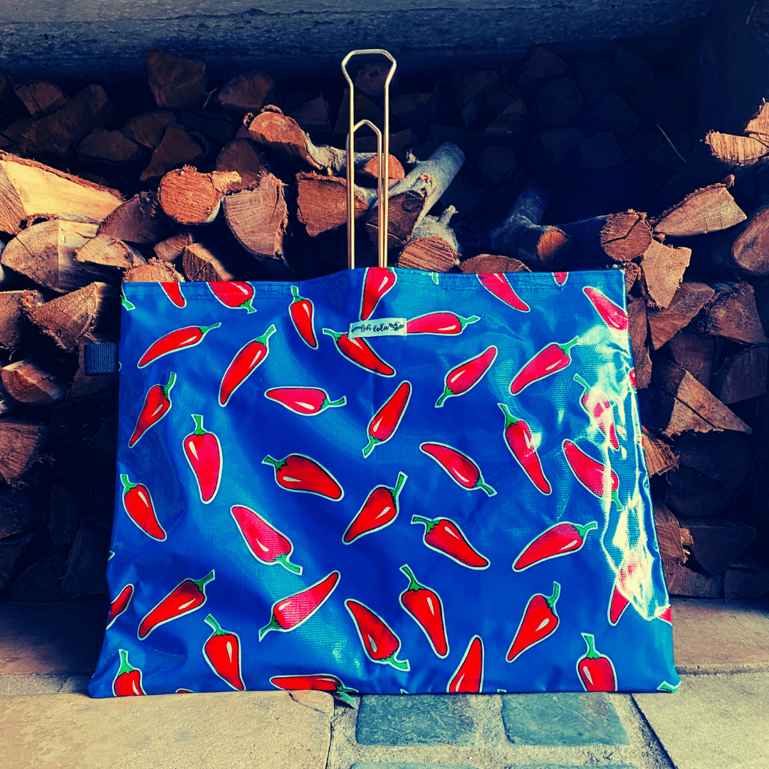 Blue bag with red chili pepper print in front of stacked firewood on stone floor