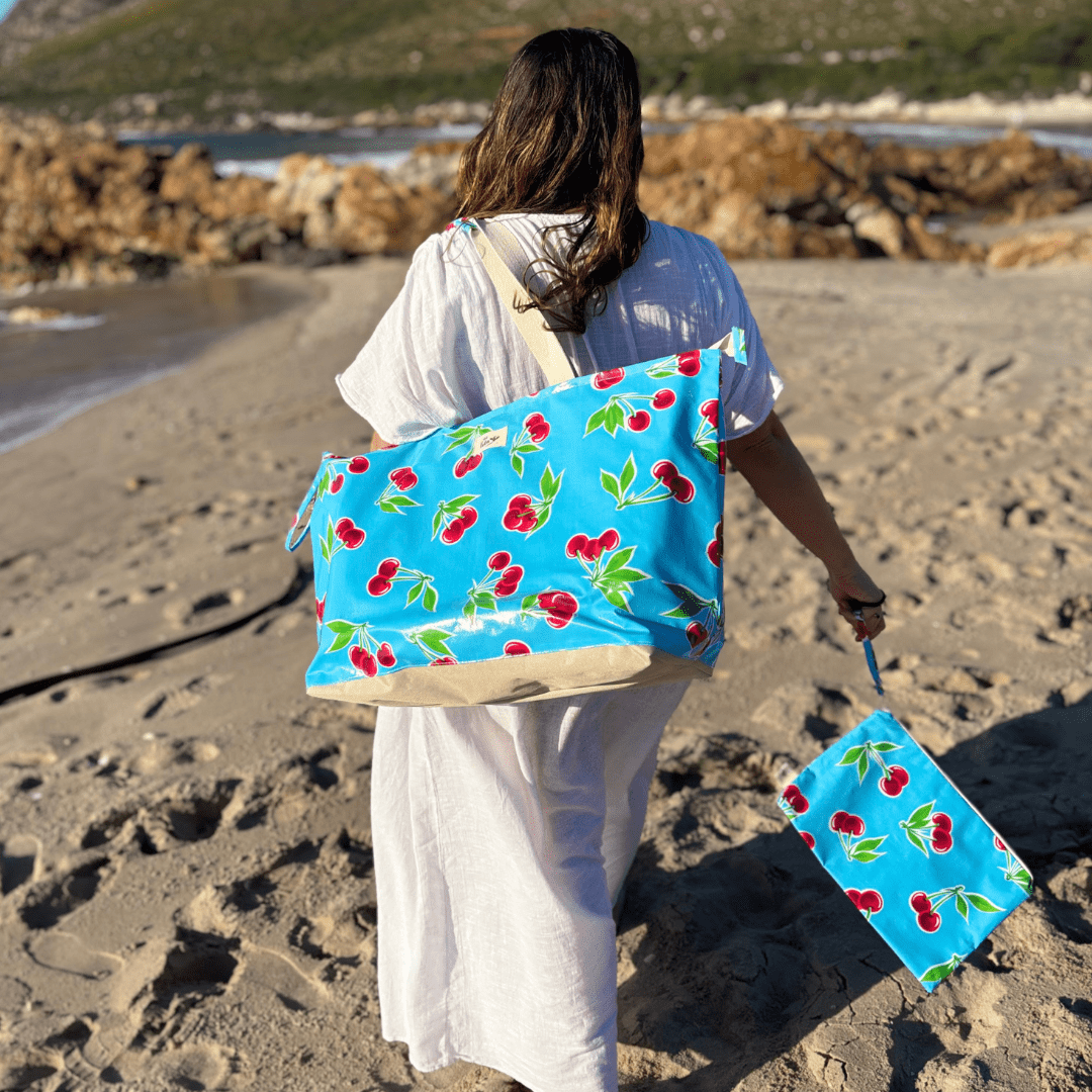 Woman in white dress on beach carrying blue cherry print tote bag and matching pouch