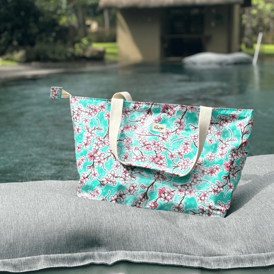 Blue floral beach tote bag with cherry blossom print on gray cushion by poolside