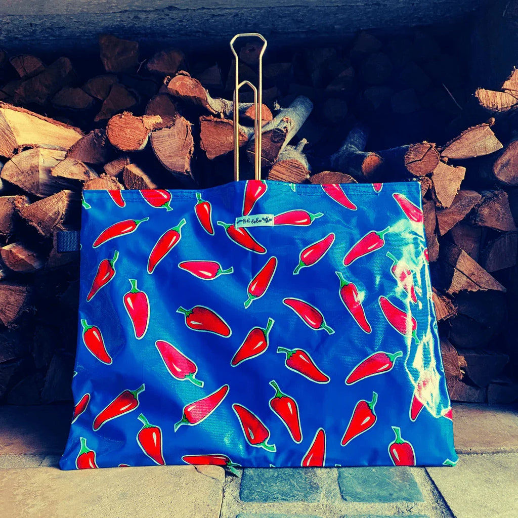 Blue bag with red chili pepper pattern against stacked firewood background