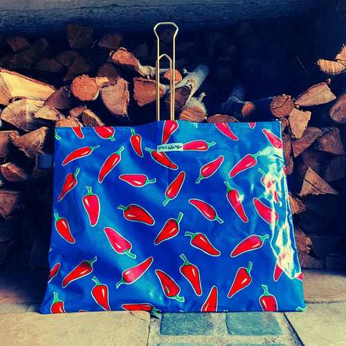 Blue bag with red chili pepper pattern against stacked firewood background