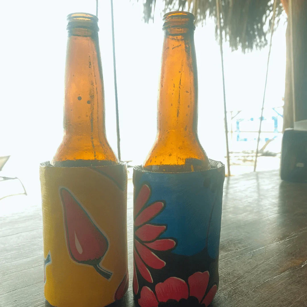Two brown beer bottles in colorful floral drink koozies on wooden table with bright outdoor background