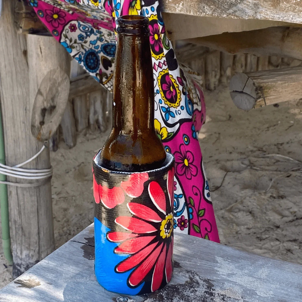 Cold beer bottle in colorful floral koozie on wooden table at sandy beach hut
