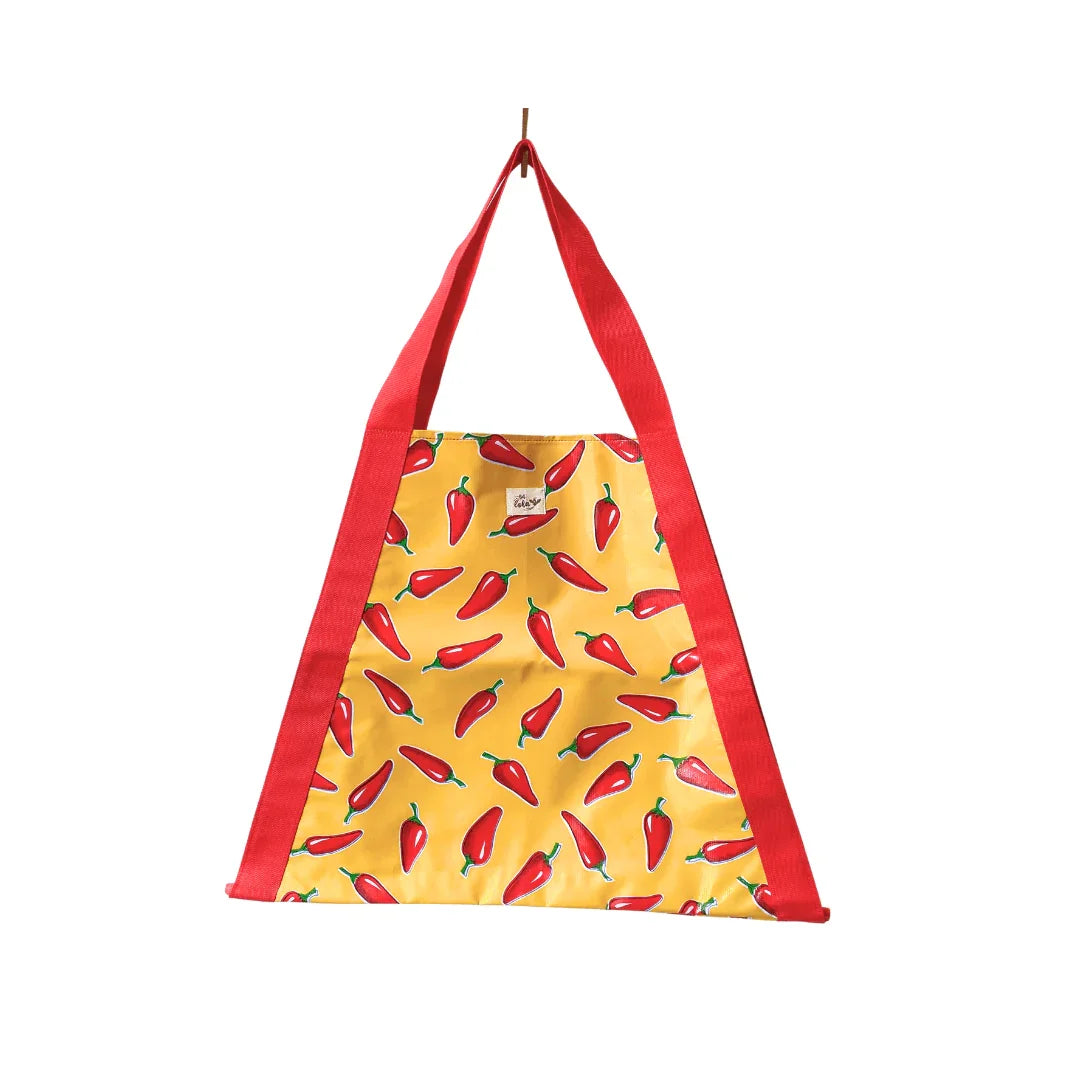 Yellow tote bag with red chili pepper print and red handles, hanging against white background