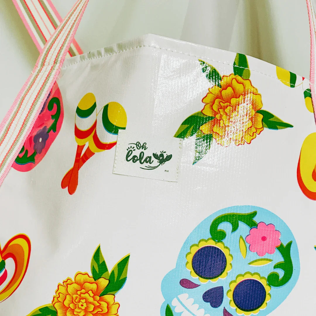 White tote bag with colorful Day of the Dead skull, yellow flowers, maracas, and striped handles
