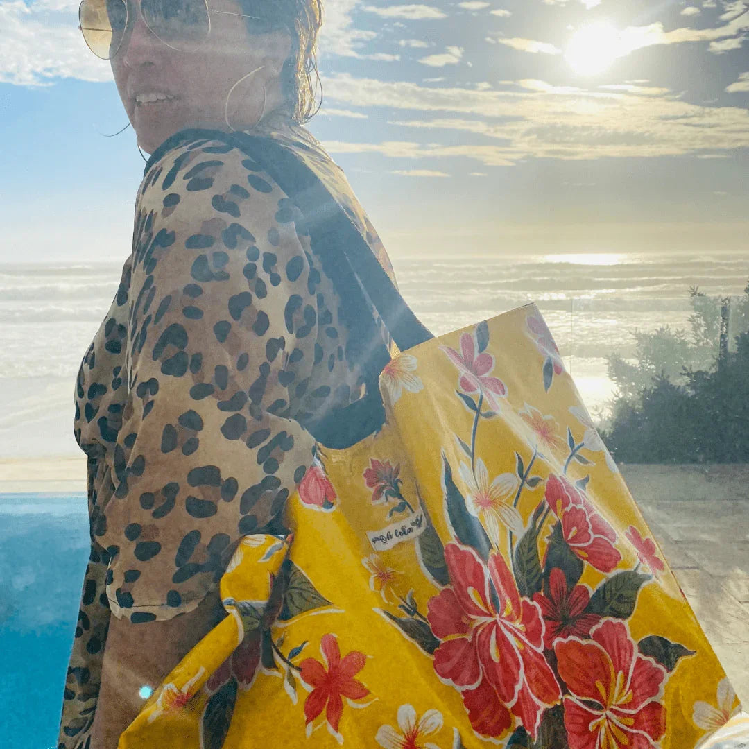 Woman in leopard print top carrying a yellow floral tote bag by the ocean at sunset