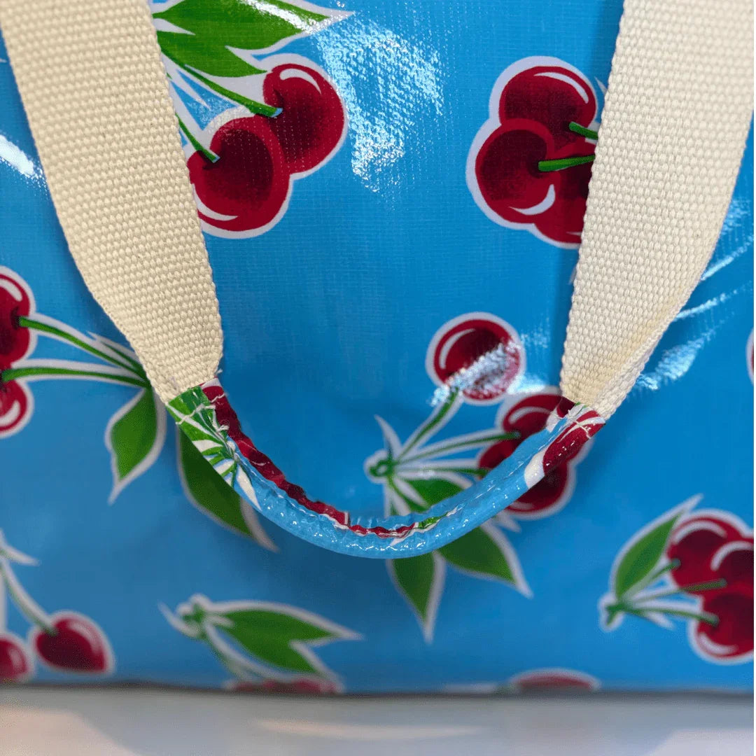 Blue tote bag with cherry print and beige canvas handles close-up