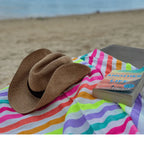 Straw hat and book on colorful striped beach towel with sandy beach background