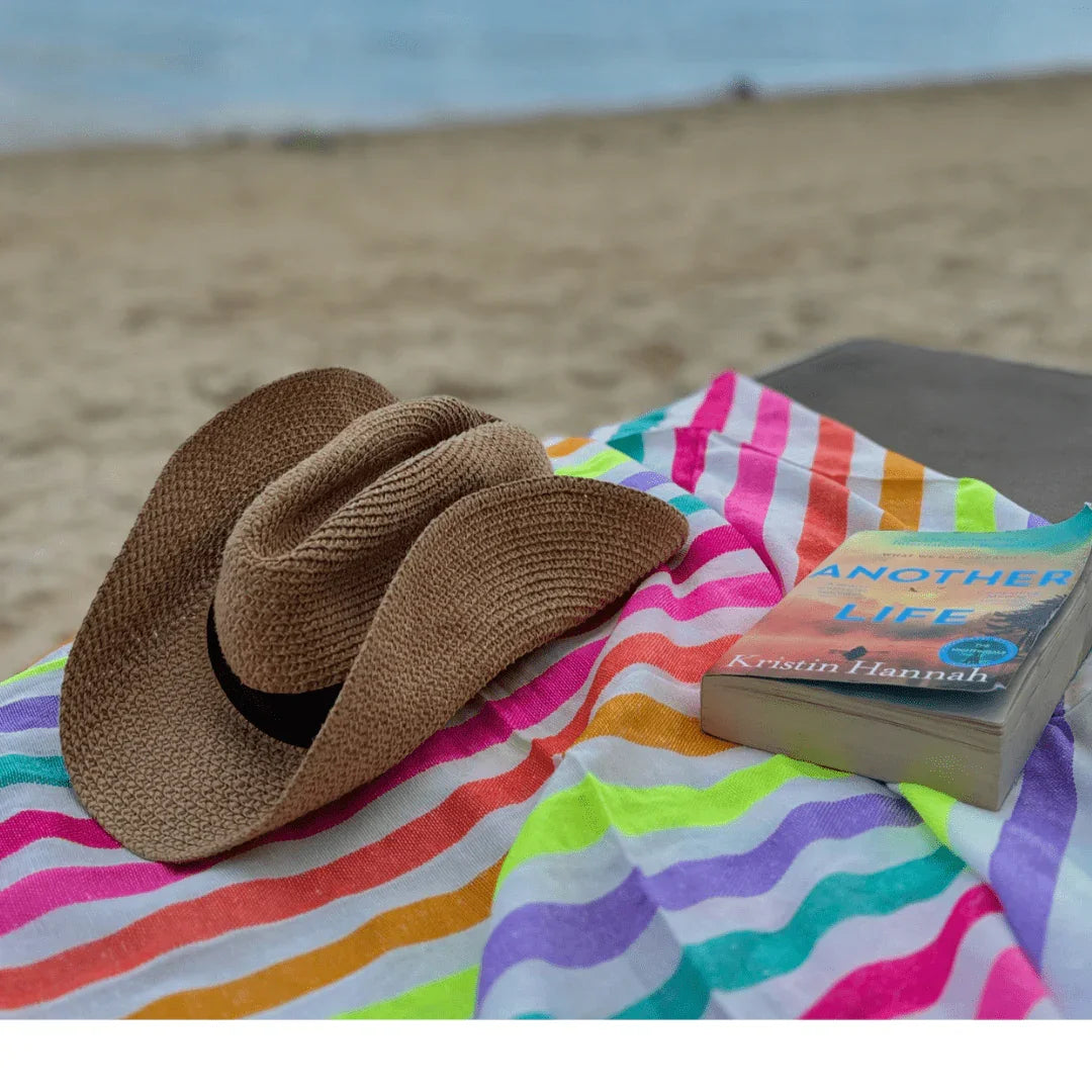 Straw hat and book on colorful striped beach towel with sandy beach background