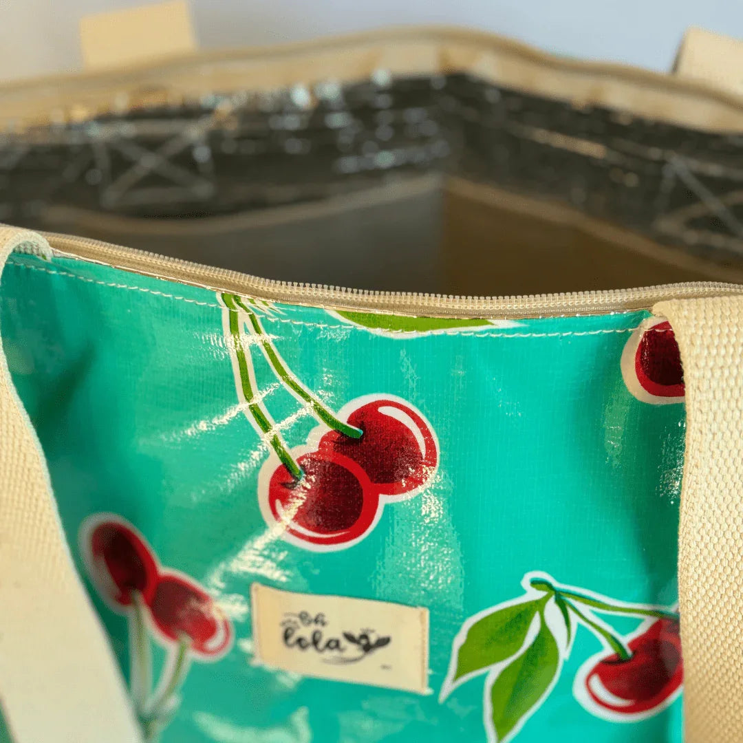 Close-up of turquoise tote bag with glossy cherry print and beige handles, unzipped opening showing interior