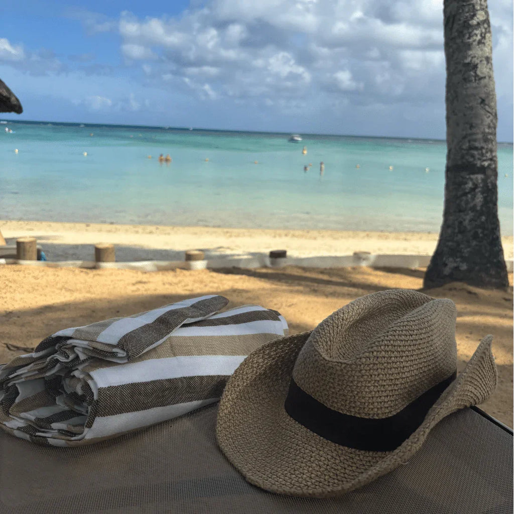 Straw hat and striped beach towel on lounge chair with tropical sandy beach and ocean background