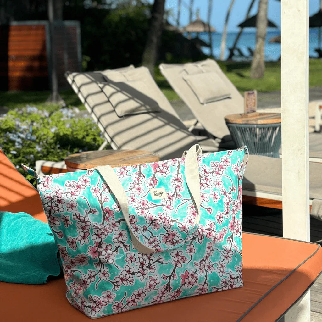 Floral print tote bag on orange pool lounge chair with blue towel and outdoor sunbeds