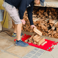 Person stacking firewood on a red mat near a stone fireplace with a woodpile