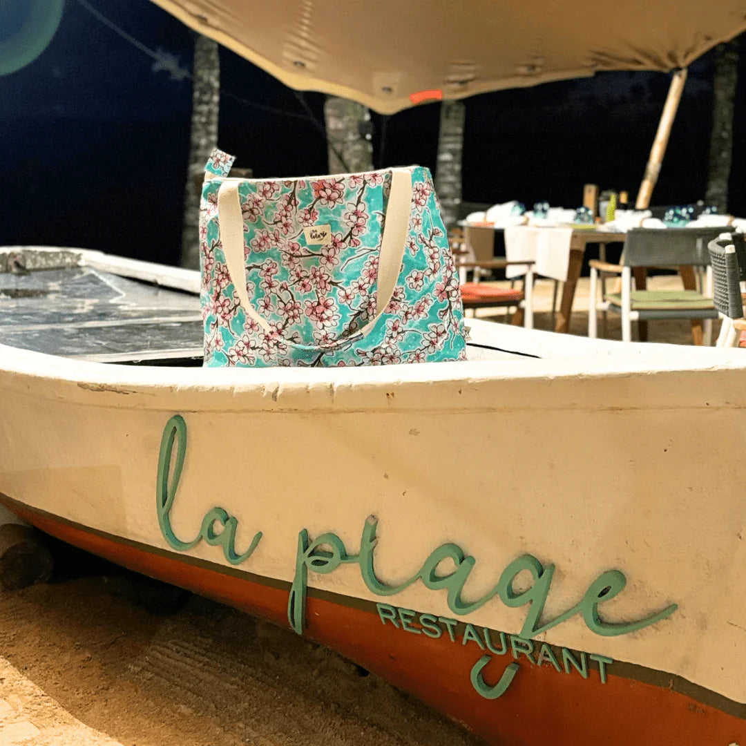 Floral tote bag inside boat with La Plage Restaurant sign at outdoor beach dining area at night
