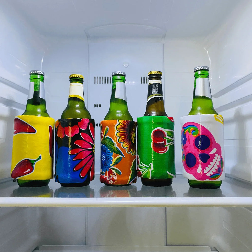 Five green beer bottles in colorful fabric koozies with chili, floral, cherry, and skull designs inside a refrigerator