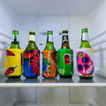 Five green beer bottles in colorful fabric koozies with chili, floral, cherry, and skull designs inside a refrigerator