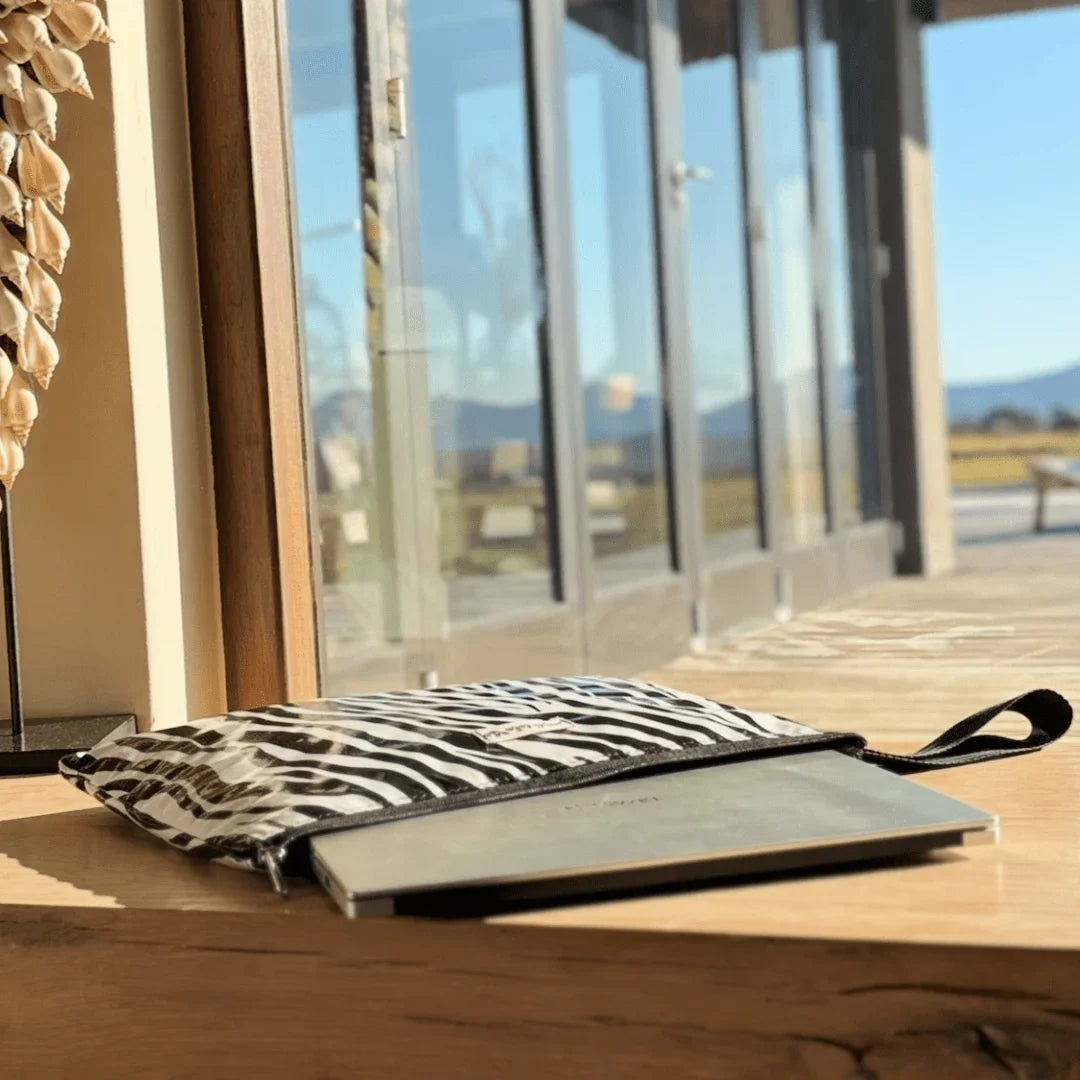 Zebra print laptop sleeve partially open with laptop inside on wooden surface near glass doors